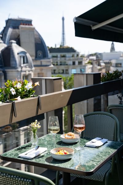 Rooftop terrace dining with wine glasses and dishes on green marble table overlooking Eiffel Tower at Warwick Paris Champs Elysées