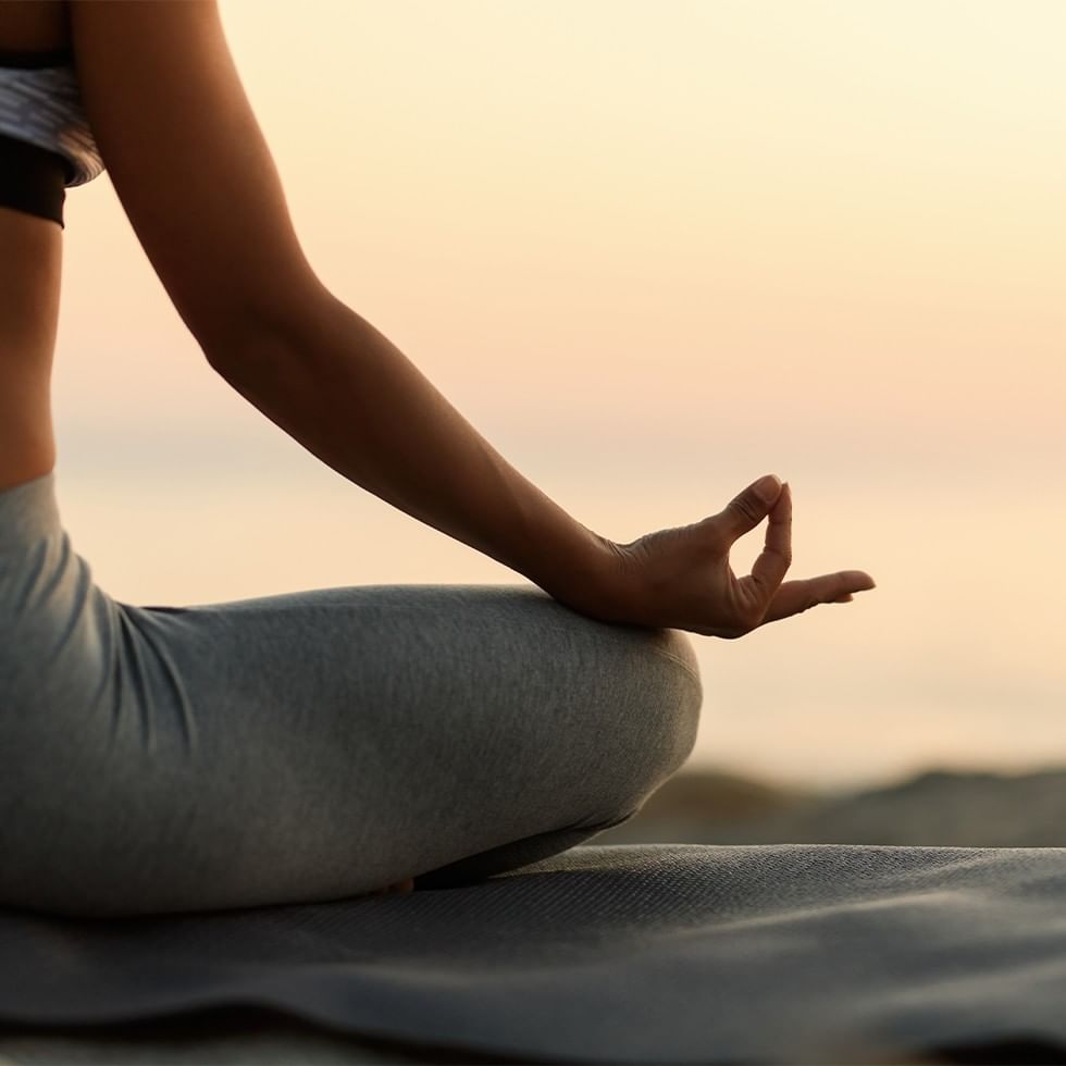 Donna seduta in meditazione yoga all'aperto con tramonto sullo sfondo.