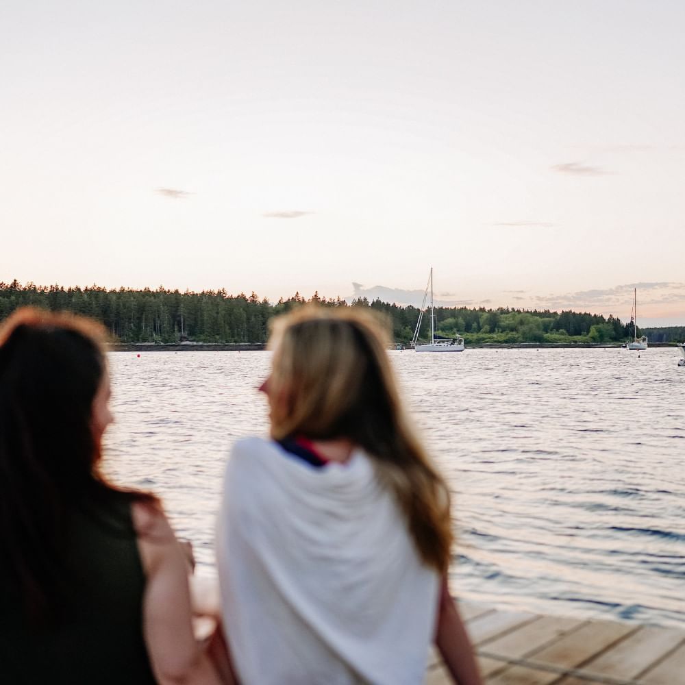 Two ladies sitting & enjoying the view from a jetty at Sebasco Harbor Resort