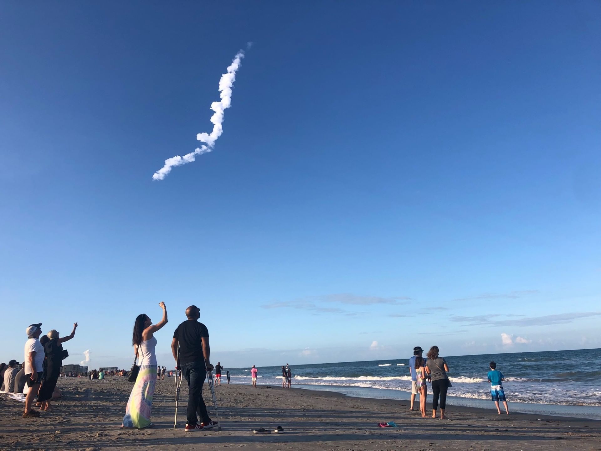 A crowd of people look up at a line of clouds from a rocket launch on Cocoa Beach, one of the best beaches near Orlando.