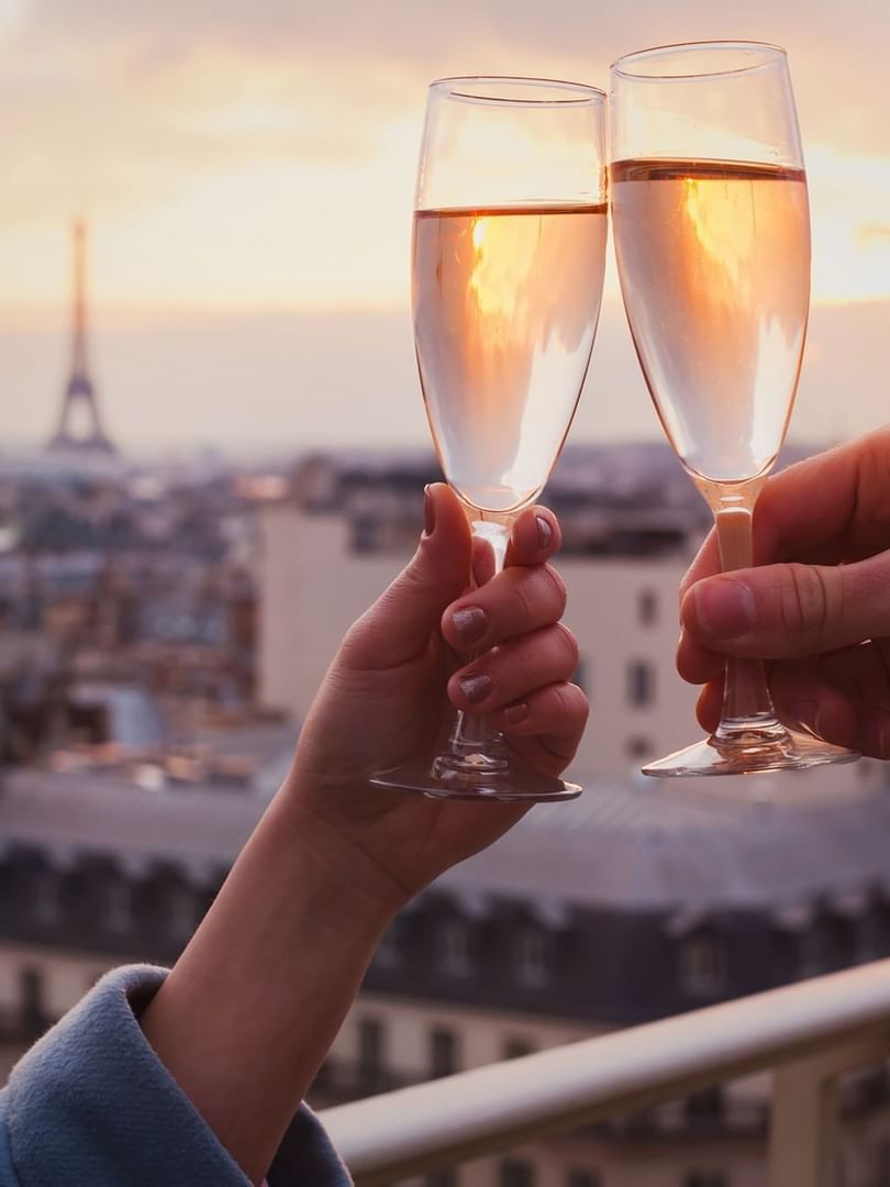 Des mains levant des coupes de champagne près de la balustrade d'un balcon, avec la Tour Eiffel en arrière-plan, à l'Hôtel Westminster de Paris