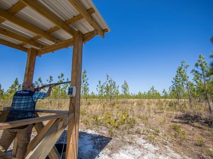 Guest aiming shotgun at outdoor sporting clay range surrounded by pine trees at Camp Creek Inn in Inlet Beach