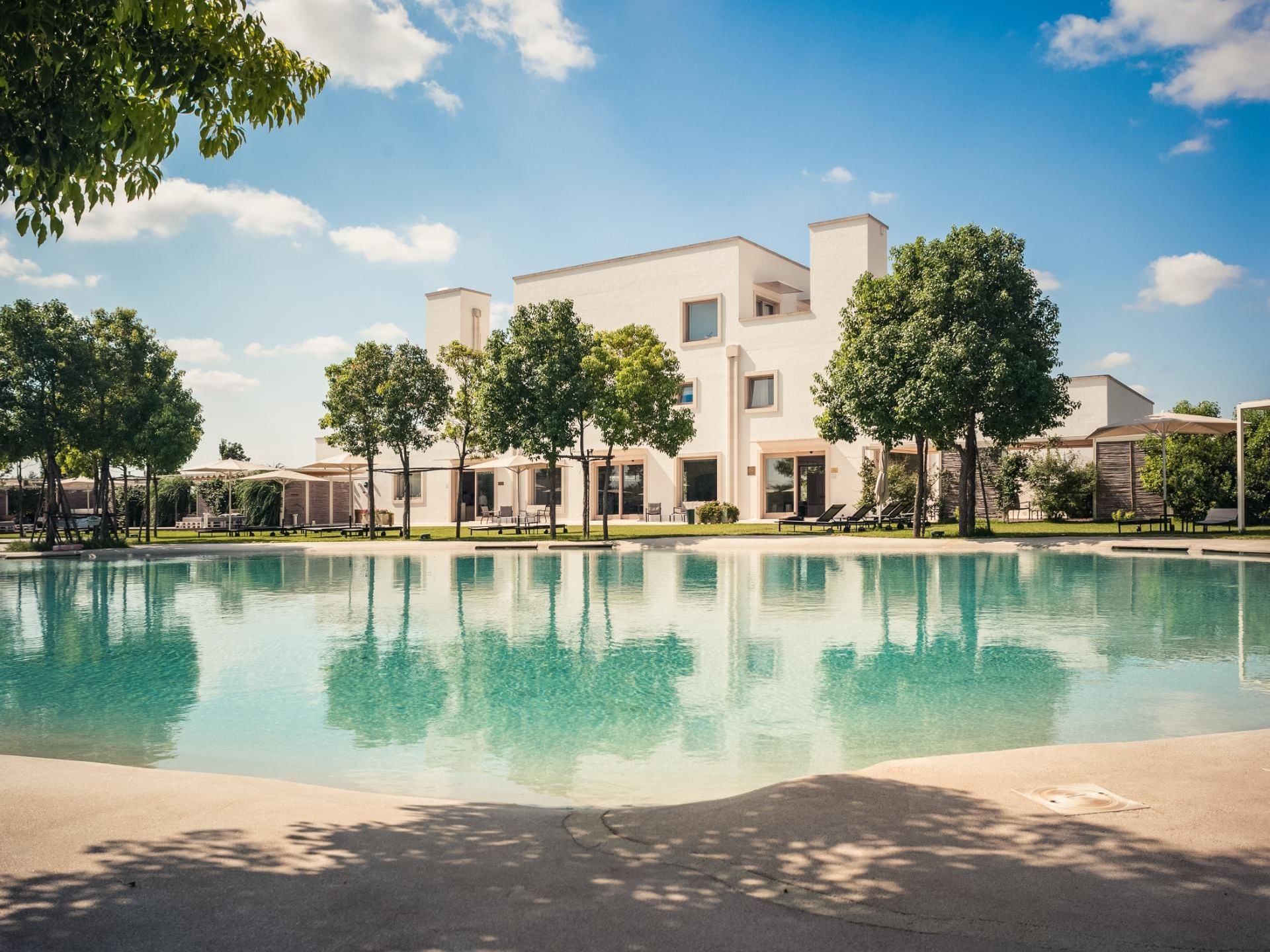 Modern Furnirussi Tenuta exterior with large pool, lounge chairs, and trees under a bright blue sky near AG Hotels