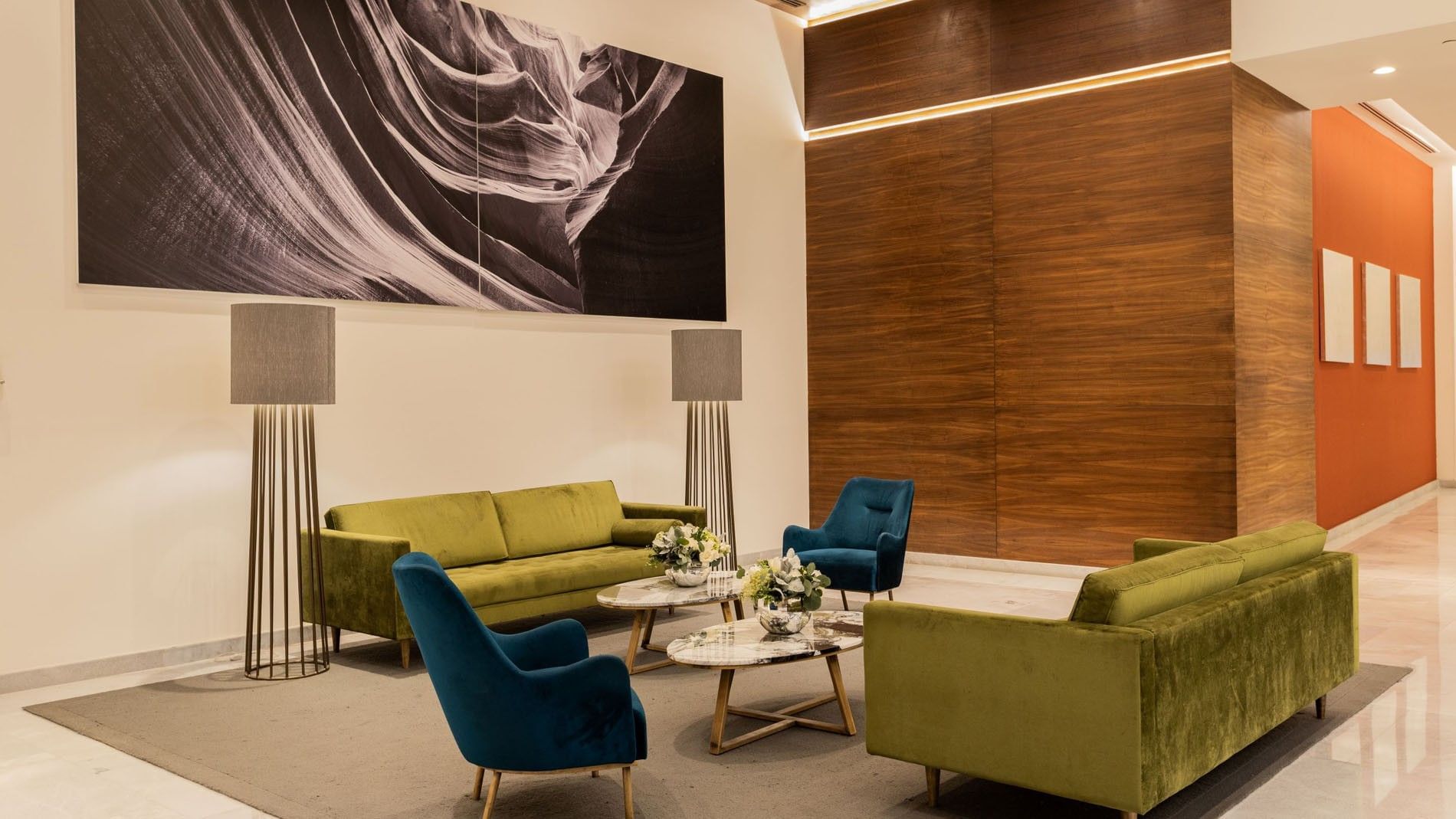Modern hotel lobby featuring green velvet sofas and blue armchairs on a rug at Camino Real Fashion Drive, Monterrey