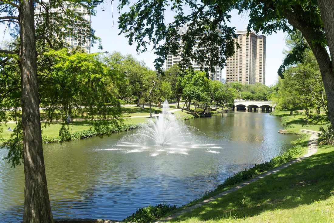 Water fountain in a pond surrounding green lawns under city skyscrapers near Warwick Melrose Dallas