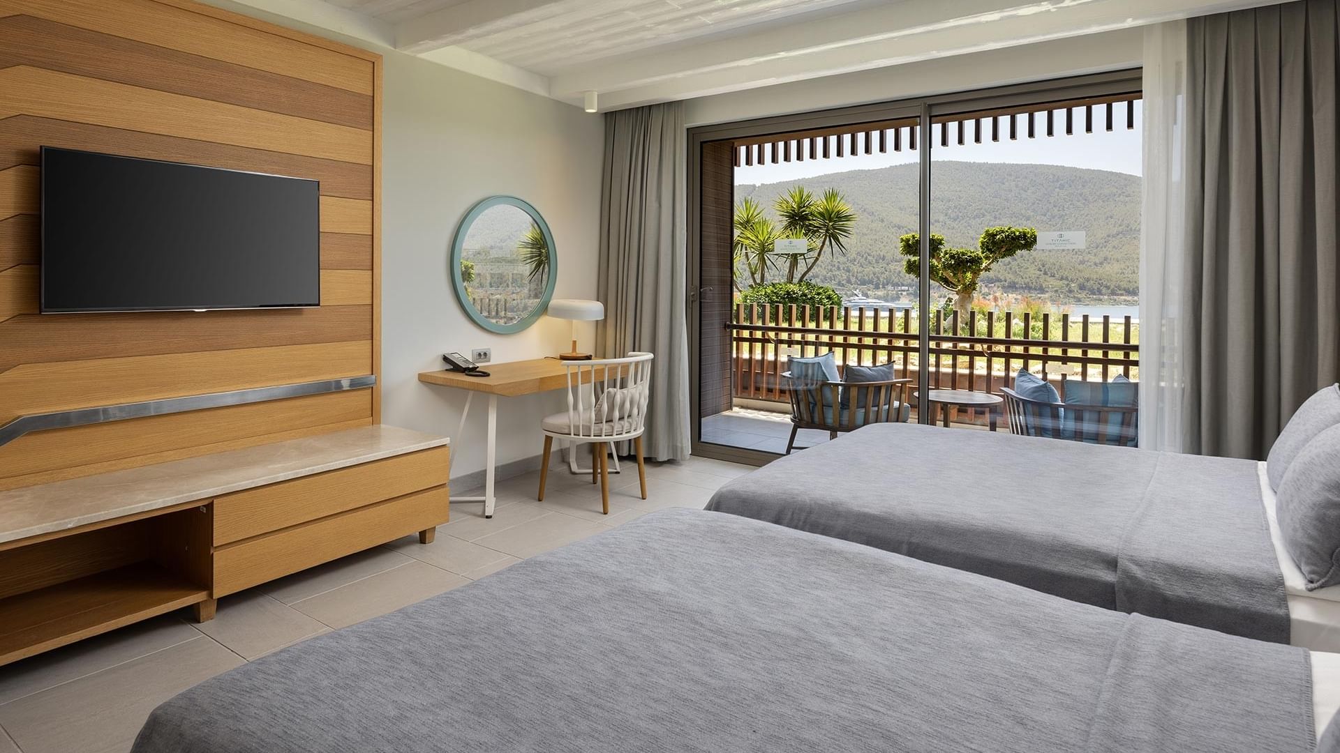 İki yataklı, çalışma masalı, TV’li ve yeşilliklere bakan balkonlu kısmi deniz manzaralı oda Titanic Luxury Collection Bodrum.