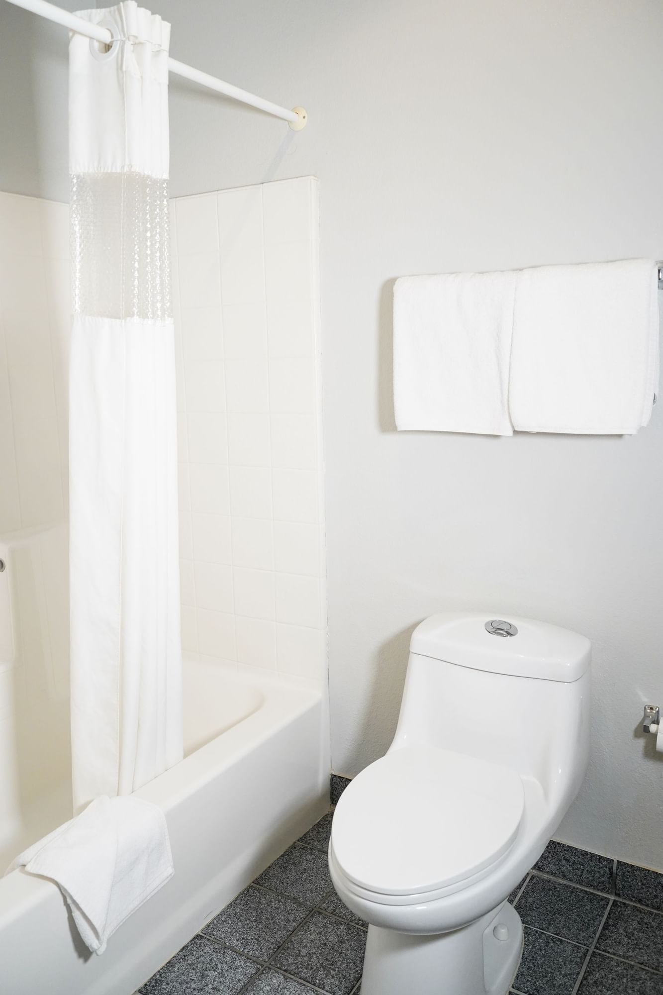 A clean and simple bathroom with a white toilet, bathtub, and gray tiles.