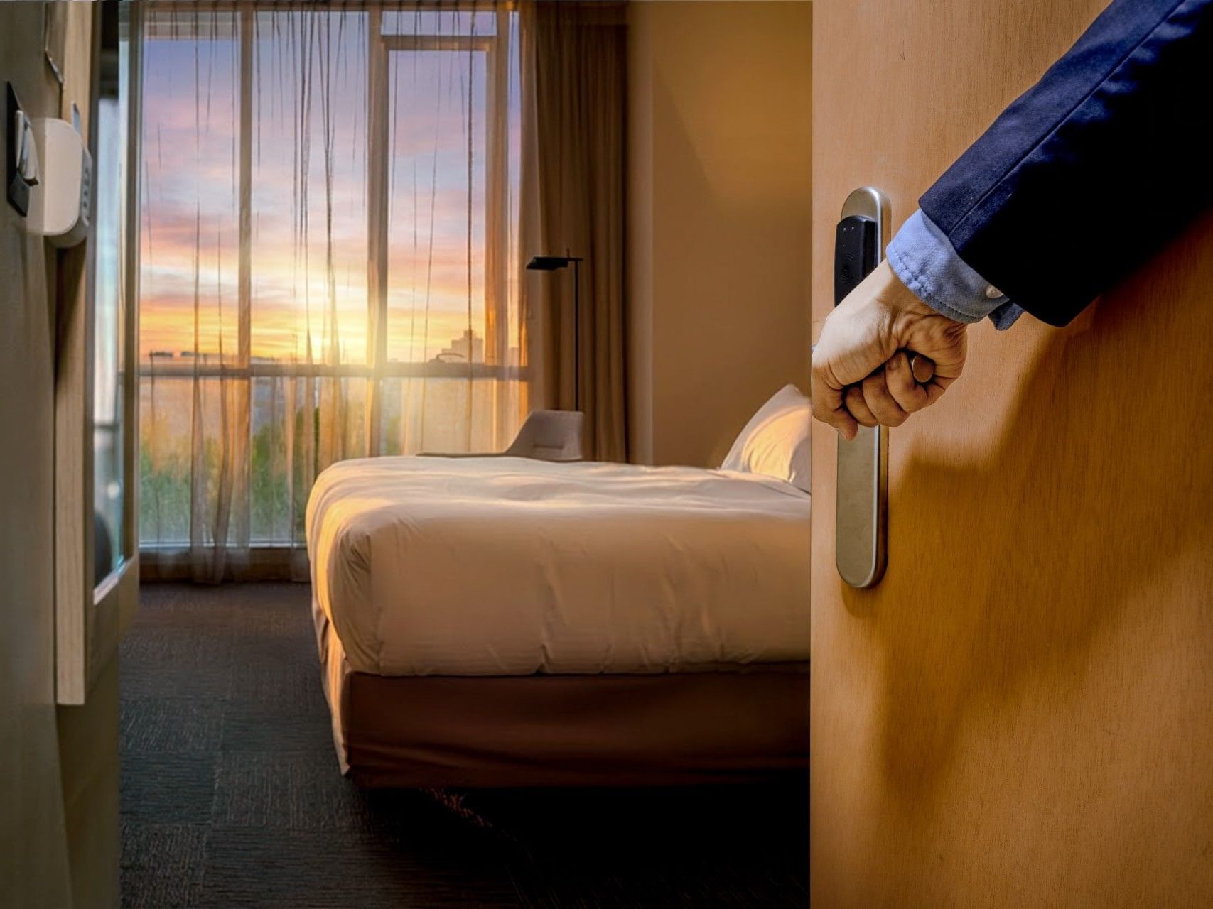 Una mano abriendo la puerta de una habitación de hotel con vistas a la puesta de sol a través de la ventana en el hotel HCC Costanera Concepción.