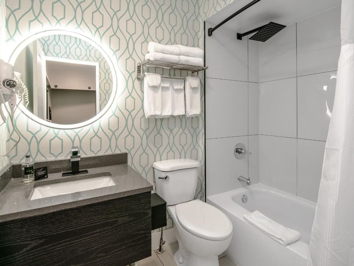 Modern bathroom with a round mirror, sink, toilet, and bathtub with a shower.