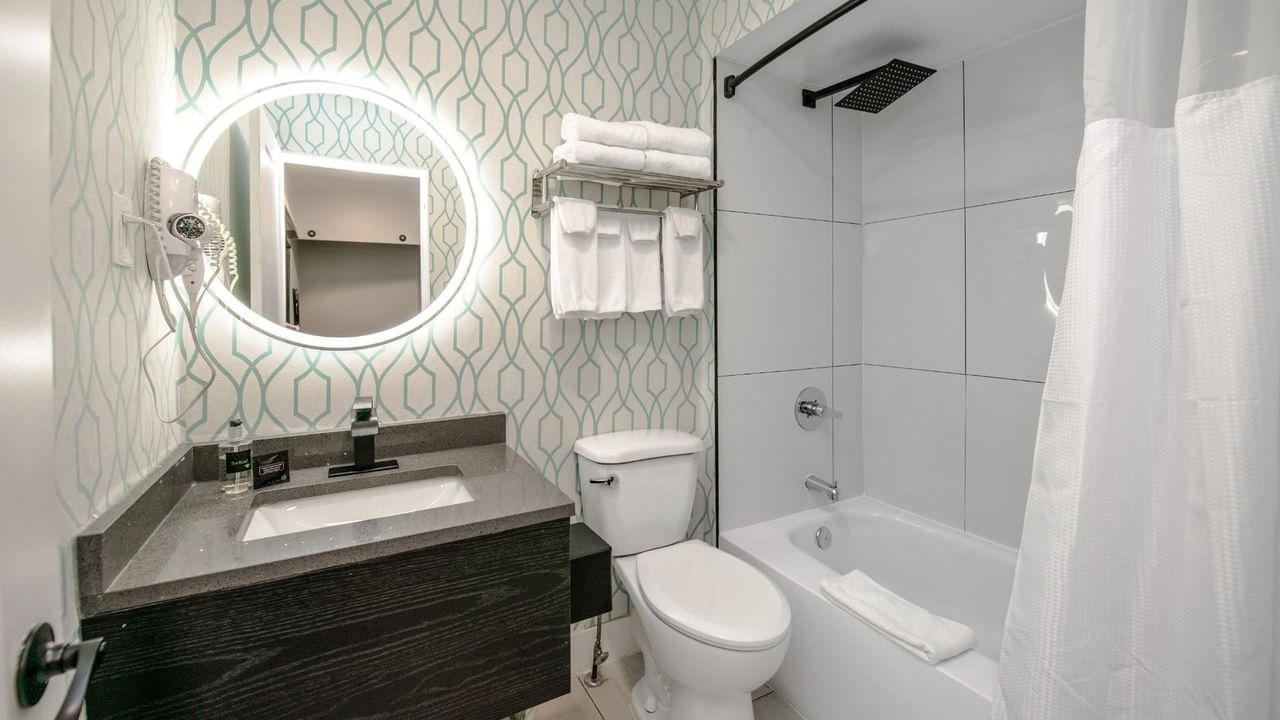 Modern bathroom with a round mirror, sink, toilet, and bathtub with a shower.