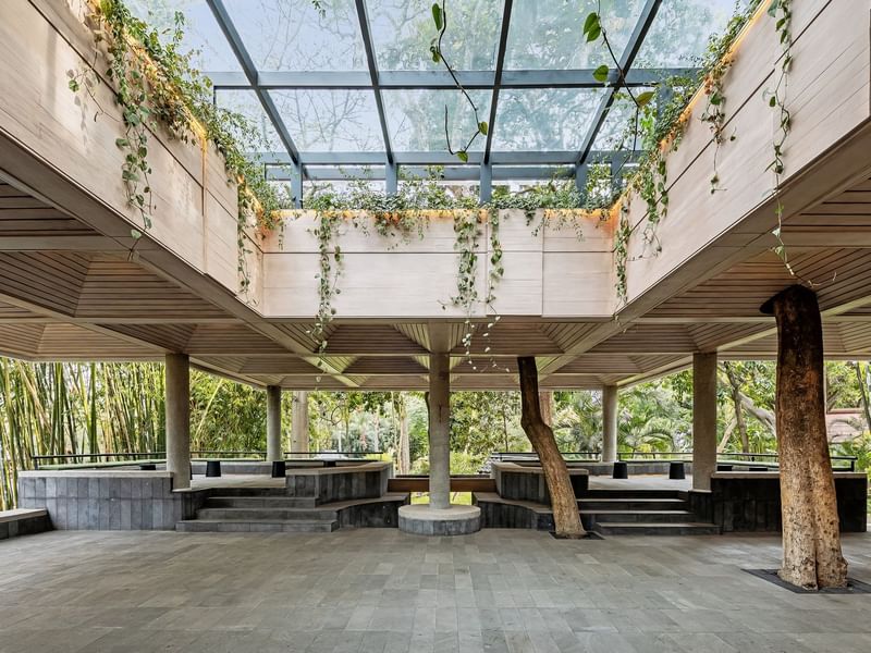 Open-air pavilion with glass ceiling, rustic tree columns, and stone seating at Grand Fiesta Americana