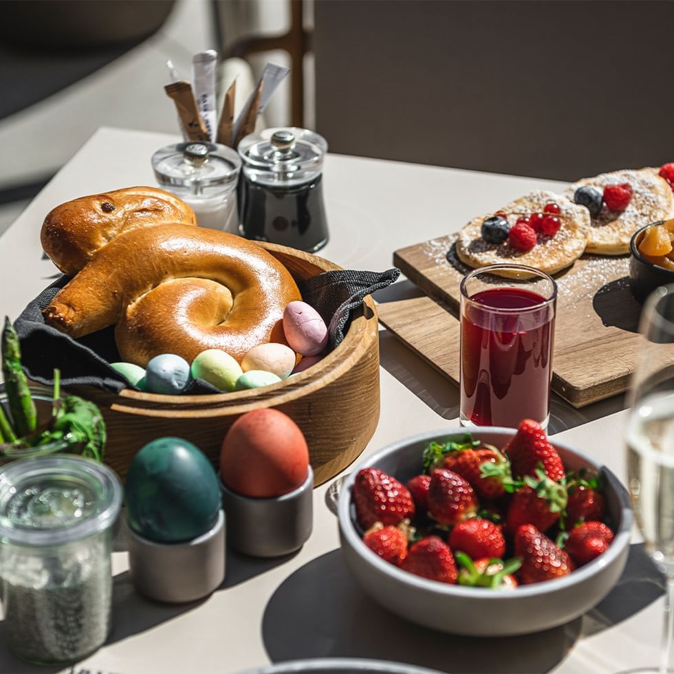 Breakfast spread with pretzels, eggs, strawberries, juice, and pastries on a white table.