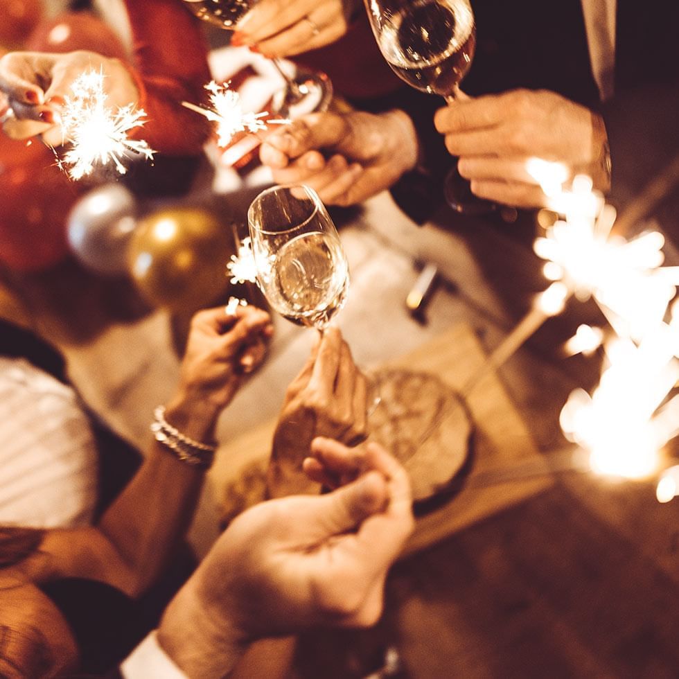 Mani che sollevano calici di vino e scintillanti fuochi d'artificio durante un brindisi festivo.
