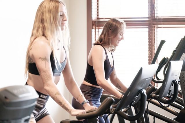 Two women exercise on treadmills in a gym.