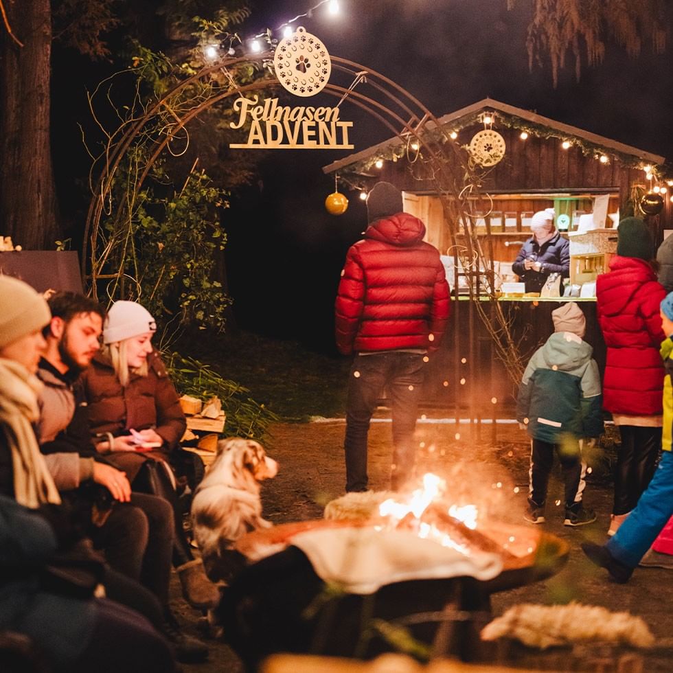 Gruppo di persone intorno a un fuoco notturno sotto un'insegna luminosa che dice Fellnasen Advent.