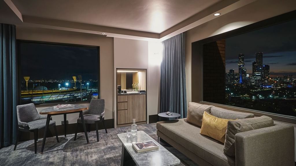 Modern suite with city skyline views, seating area, and dining space at Pullman East Melbourne