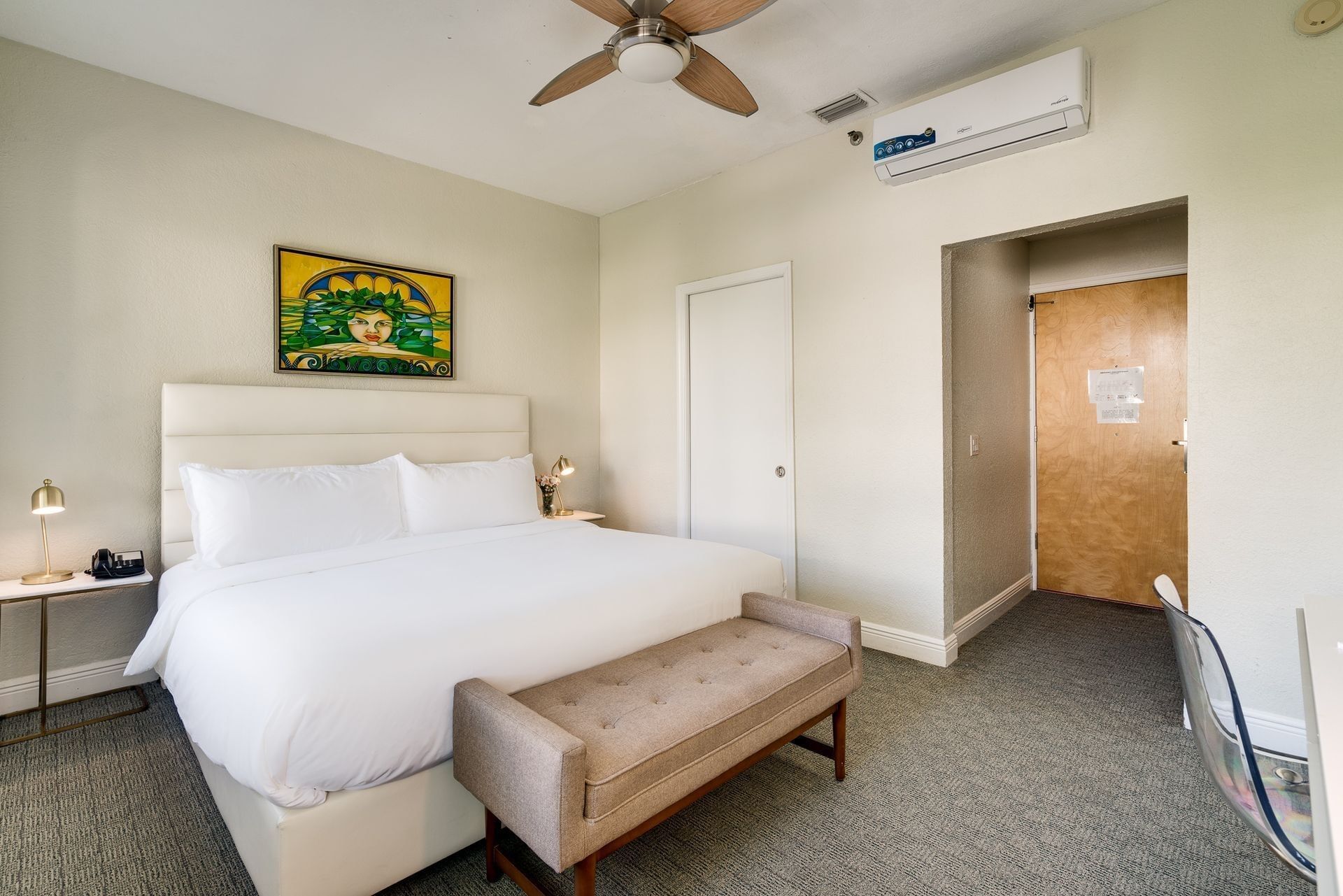 A hotel room with a bed, nightstand, and bench.