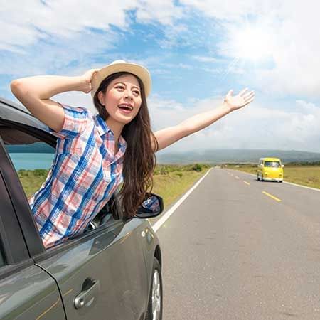 A joyful woman leans out of the car window during a road trip - Lexis Suites Penang