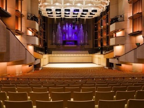 Modern concert hall interior with tiered seating, illuminated walls, and purple-lit stage at QPAC.