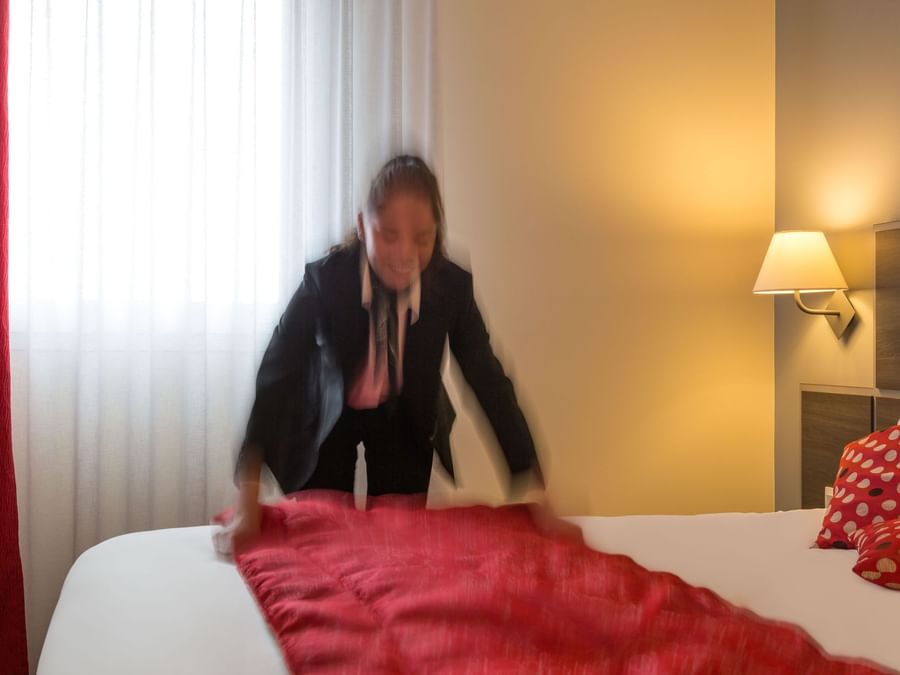 A maid preparing a bed in a room at Actuel Hotel