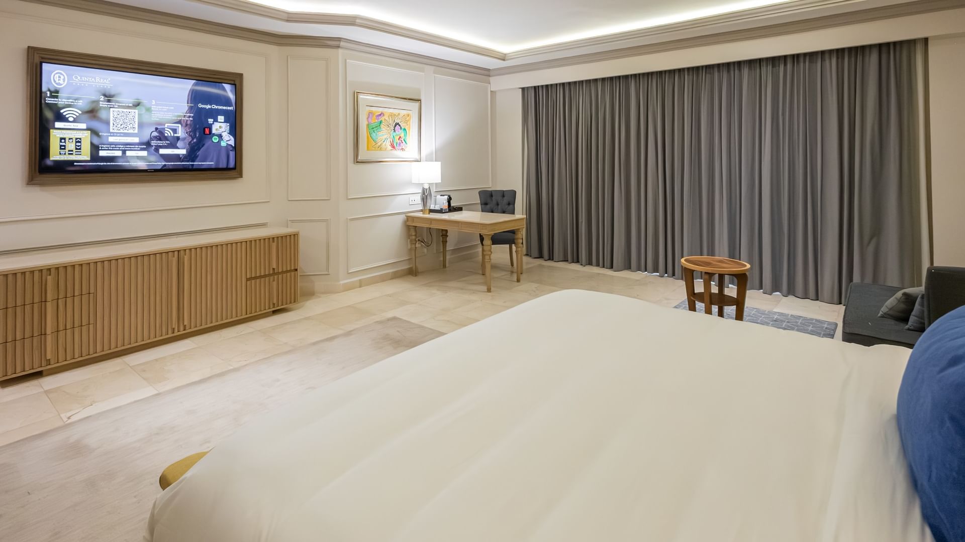 Habitación amplia con cama king size, escritorio, televisión y cortinas grises en Quinta Real Monterrey