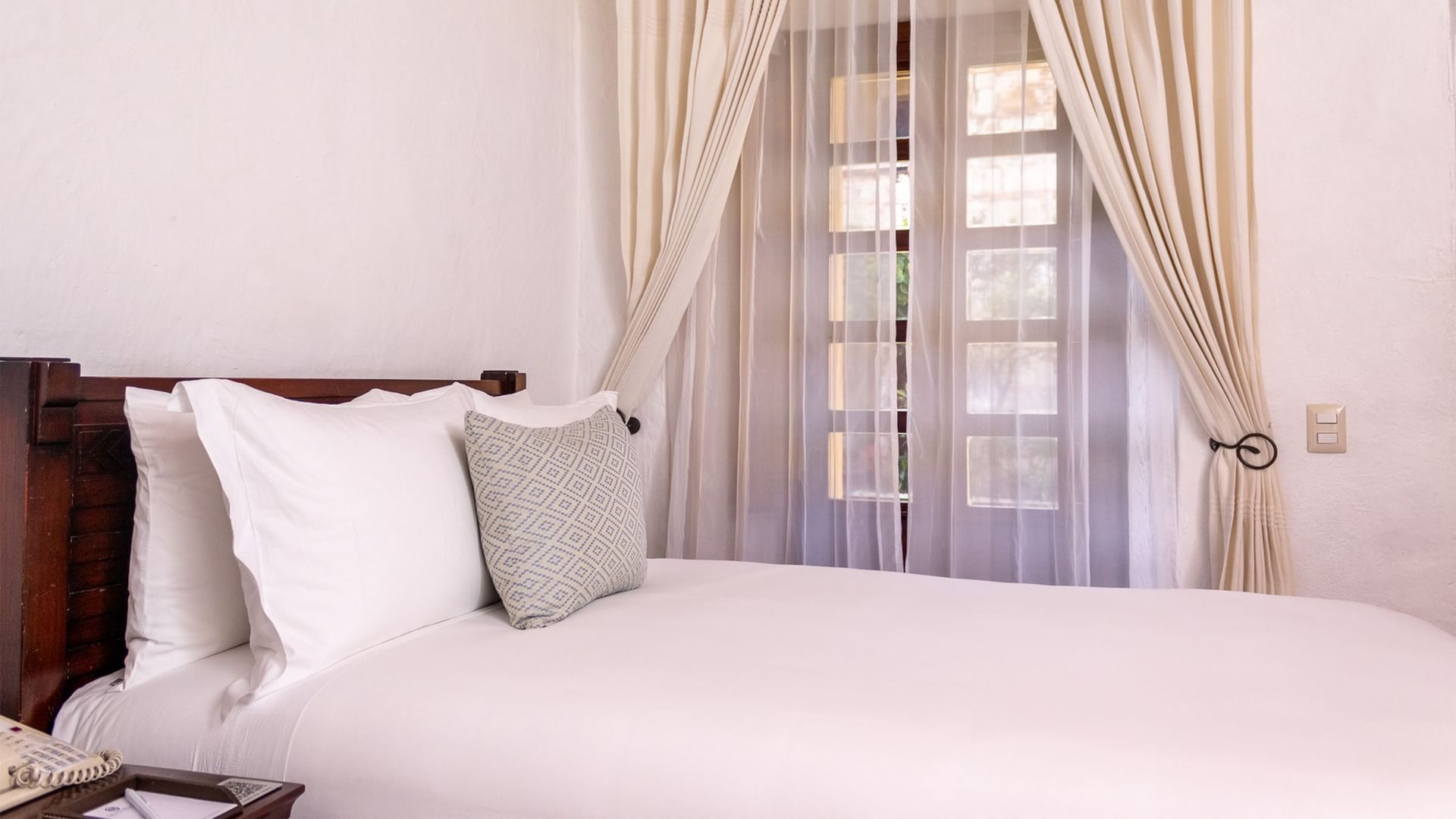White bed with three pillows and curtains at Quinta Real Oaxaca in Oaxaca de Juarez.
