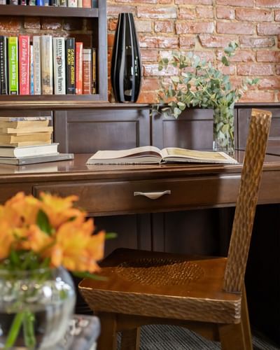 a chair faces a wooden desk with an open magazine and pile of bo
