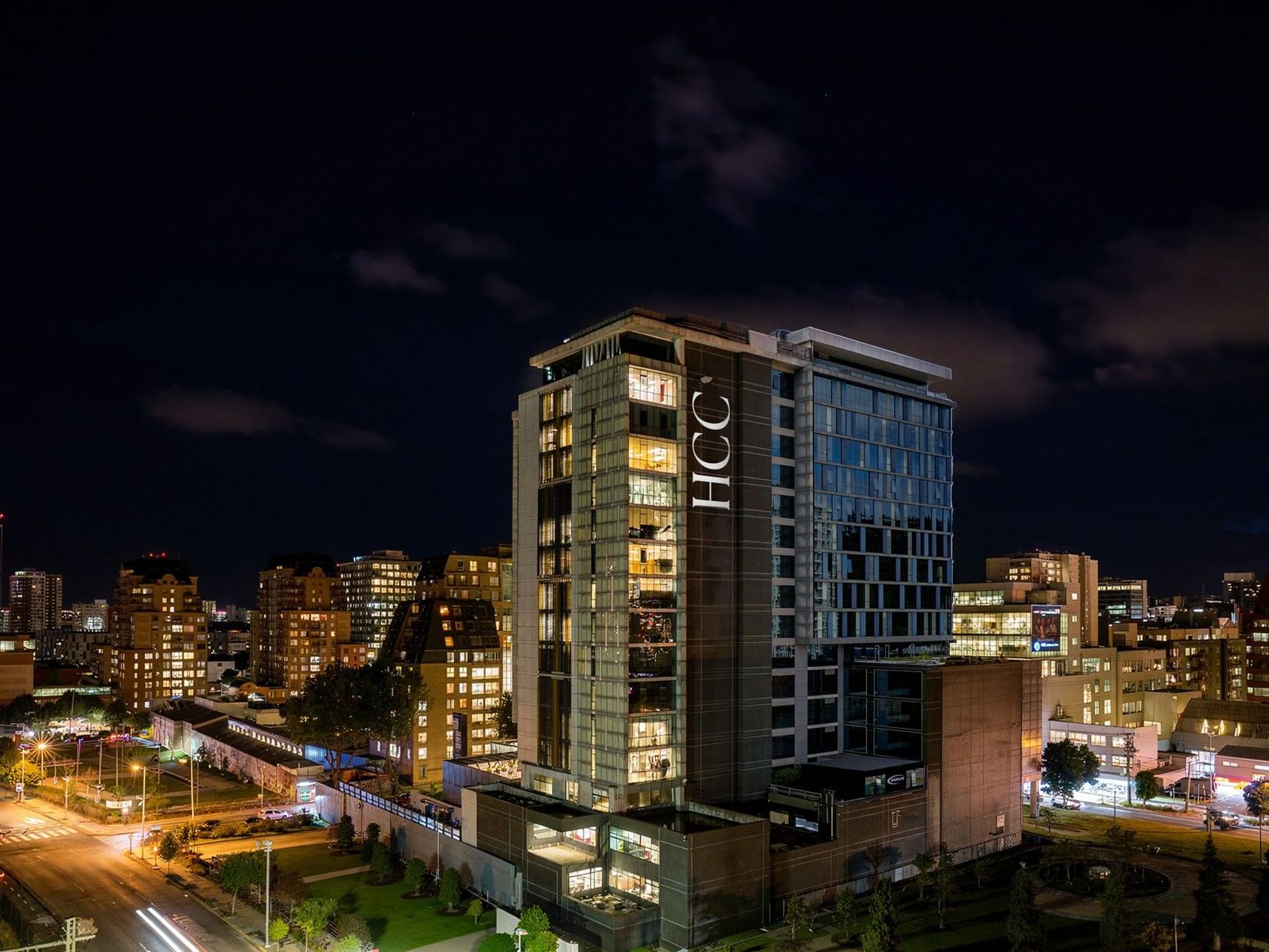 El hotel HCC Costanera Concepción iluminado por la noche en un paisaje urbano.