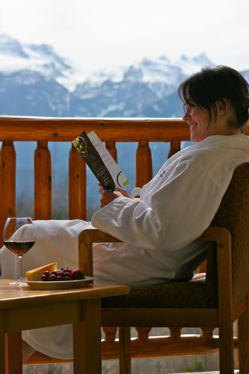 Woman in robe reading and drinking wine on balcony with view of 