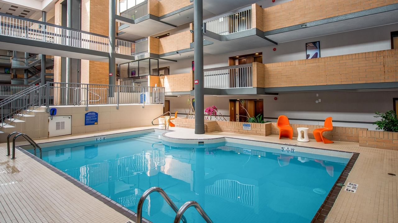 Indoor pool with bright orange seating surrounded by multi-level balconies at Coast Calgary University Area Hotel by APA