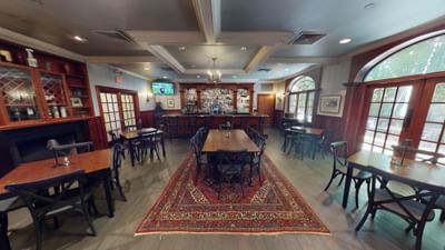 Warm pub dining room with wooden tables on a patterned red area rug facing the bar counter at the Avon Old Farms Hotel