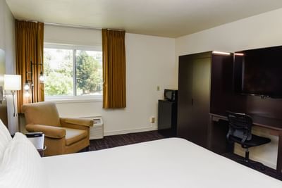 Accessible King Room featuring a bed with an armchair and a dark wardrobe by the window at Lake Natoma Inn