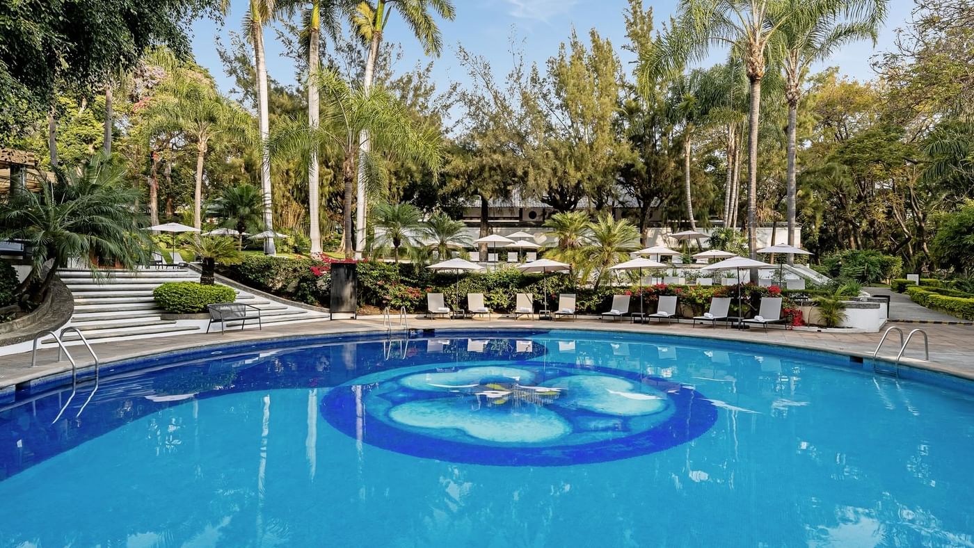 Luxurious swimming pool surrounded by lounge chairs and lush greenery at Grand Fiesta Americana