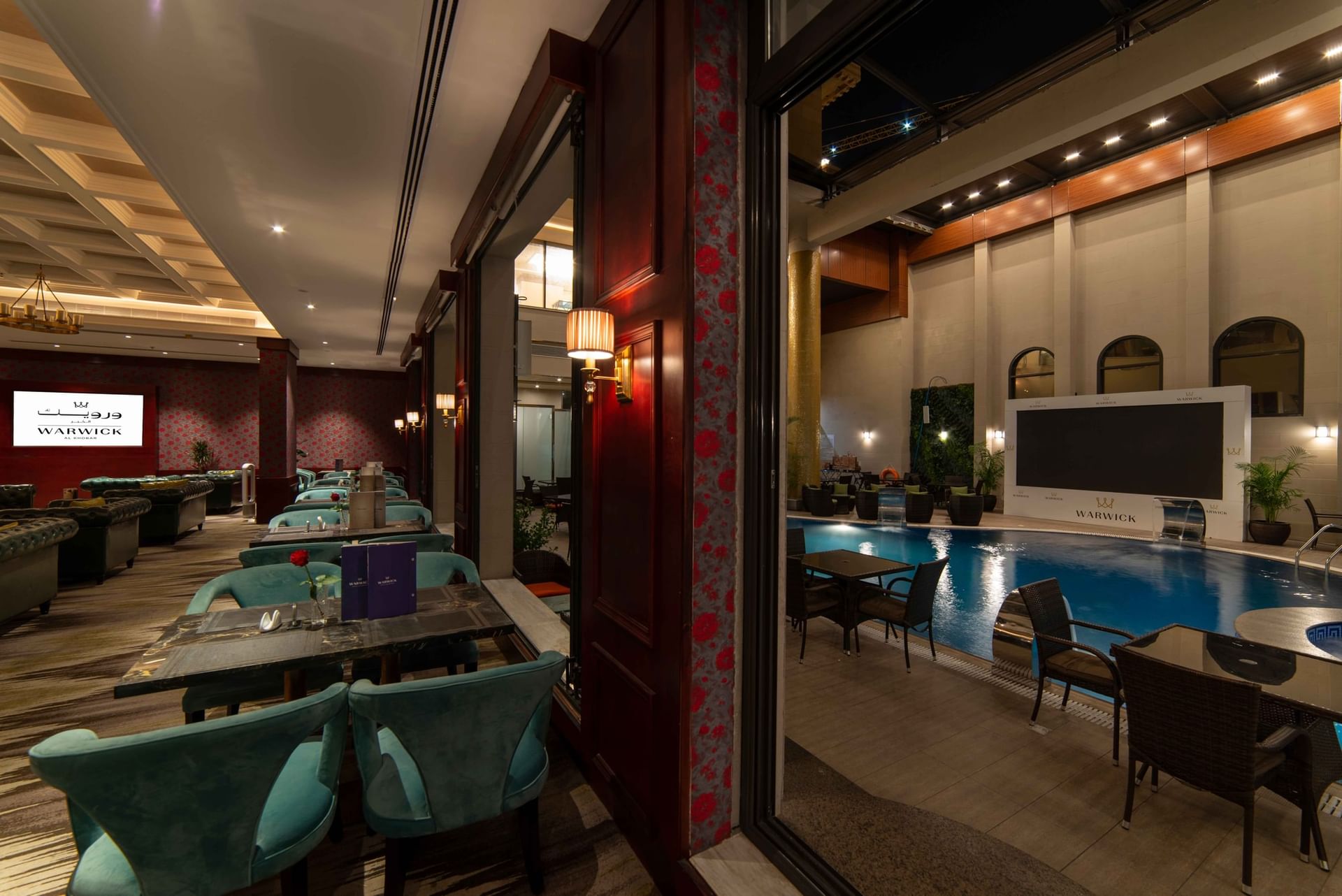 Cigar Lounge features teal chairs overlooking a blue pool through a glass partition at Warwick Al Khobar