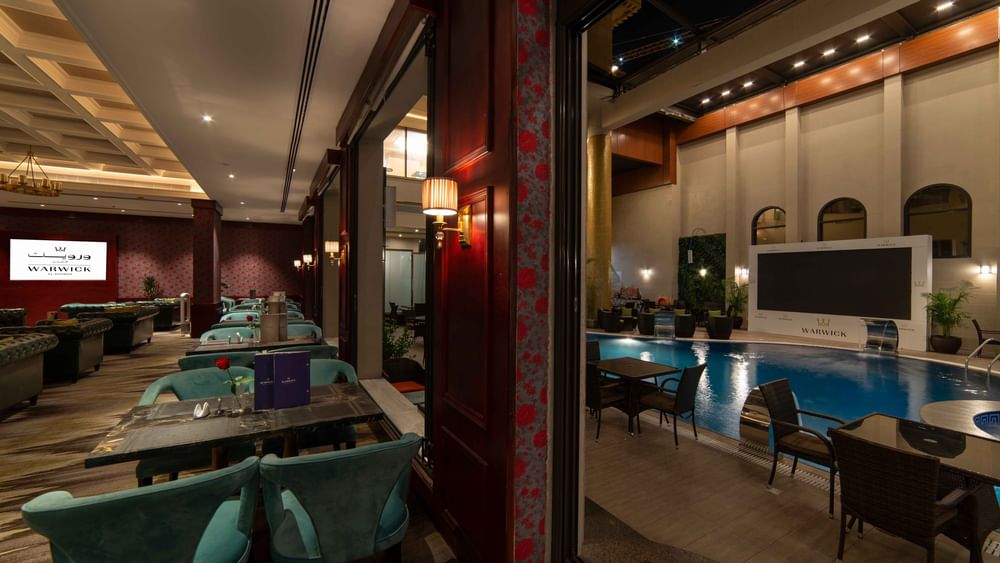 Cigar Lounge features teal chairs overlooking a blue pool through a glass partition at Warwick Al Khobar
