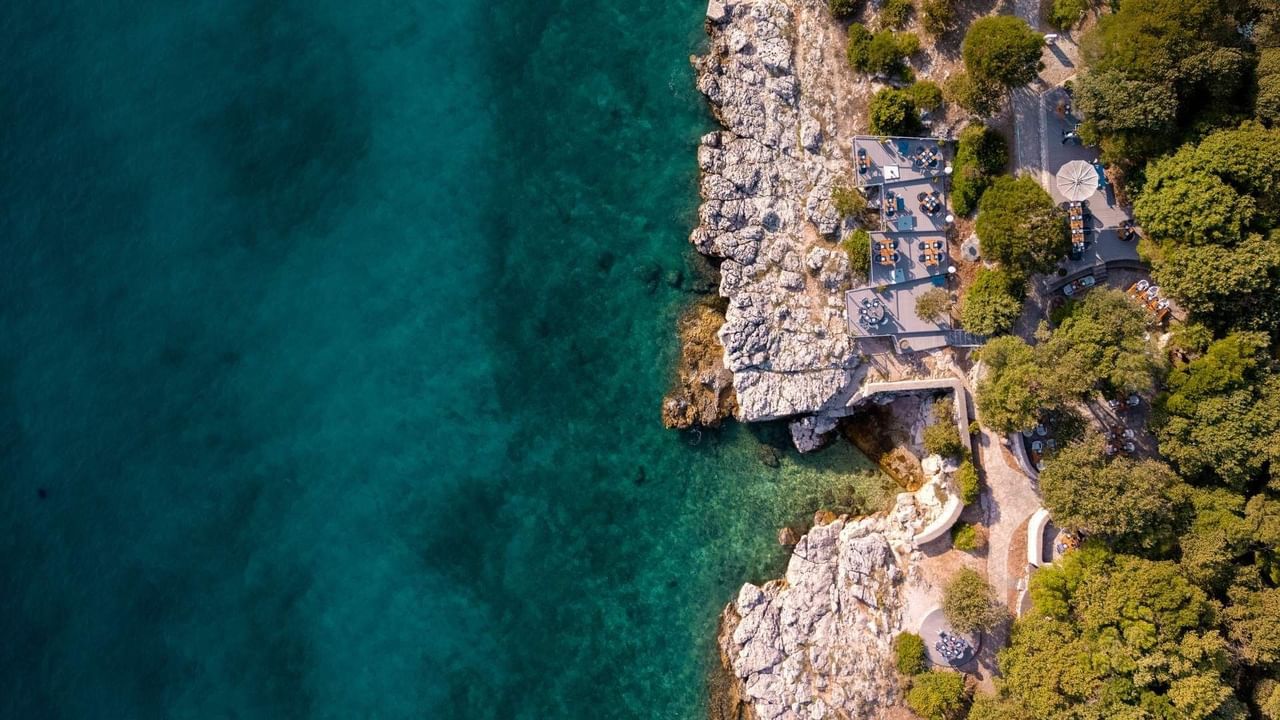 Vista aerea di una costa rocciosa con una terrazza e un percorso lastricato tra gli alberi.