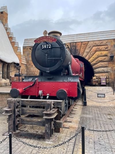 A black and red train stopped behind a small barricade with a stone archway in the background.