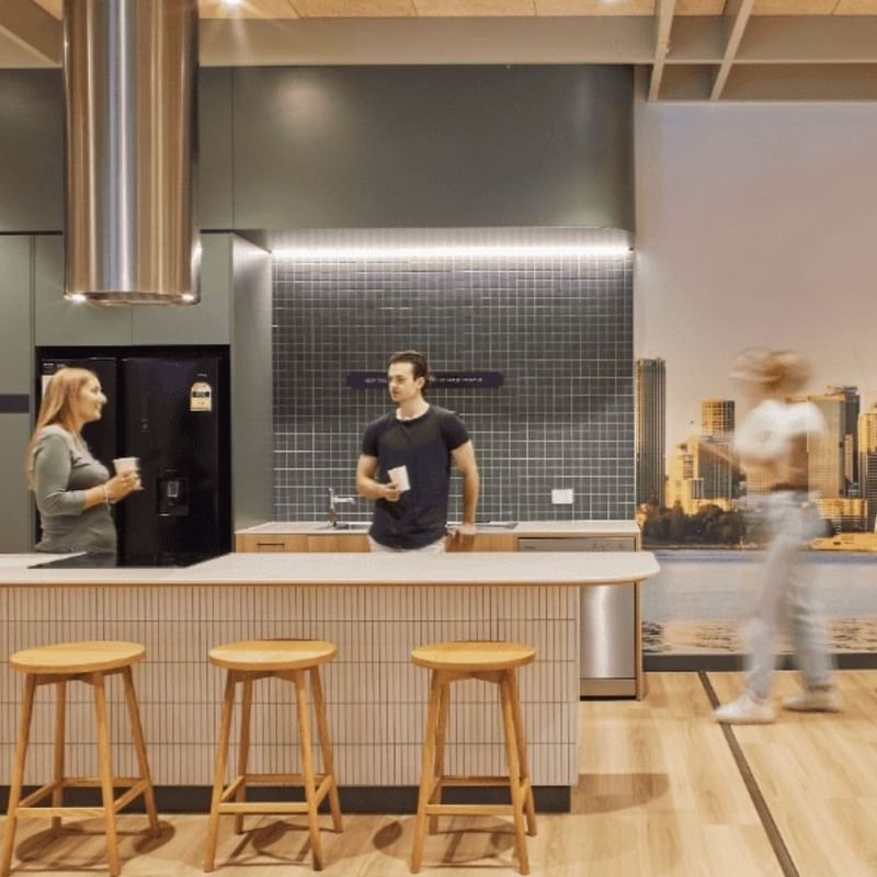 Interior of a modern kitchen with three people, wooden furniture, and a cityscape mural.