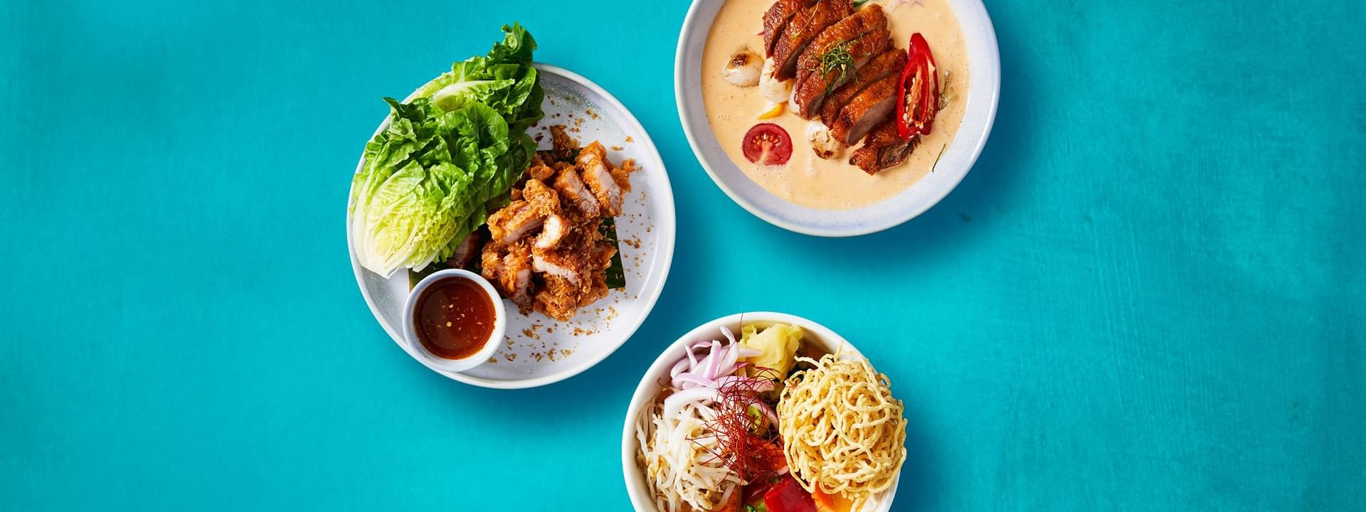 Three beautifully presented Thai dishes, featuring crispy pork and duck curry, at New Town Thai Restaurant in Novotel Sydney