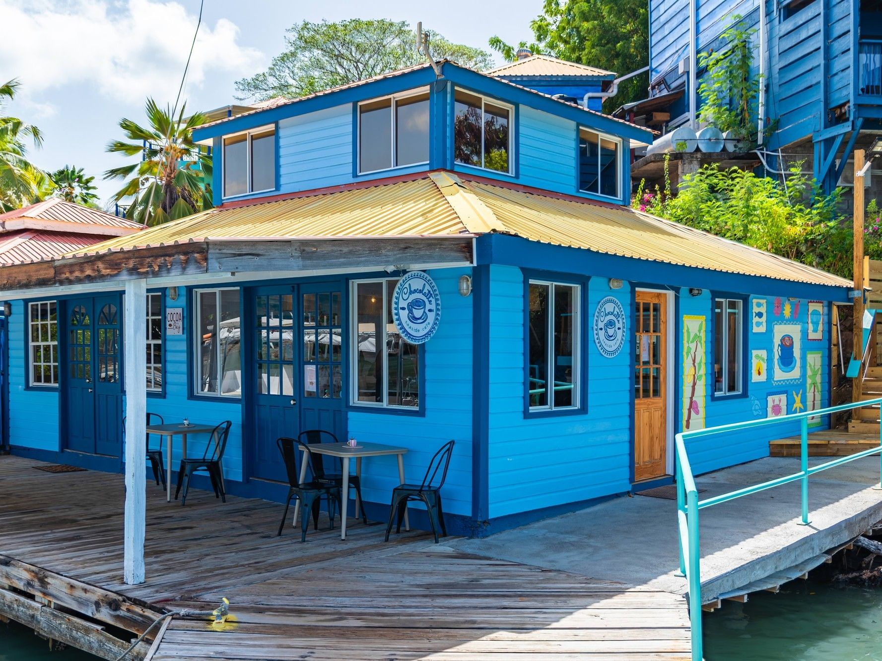 Bright blue waterfront cafe with outdoor seating on a wooden deck at True Blue Bay Boutique Resort in Saint George's