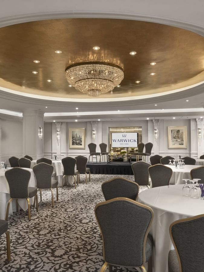 Grand ballroom with round banquet tables& chairs under a stunning gold dome and chandelier at Warwick New York