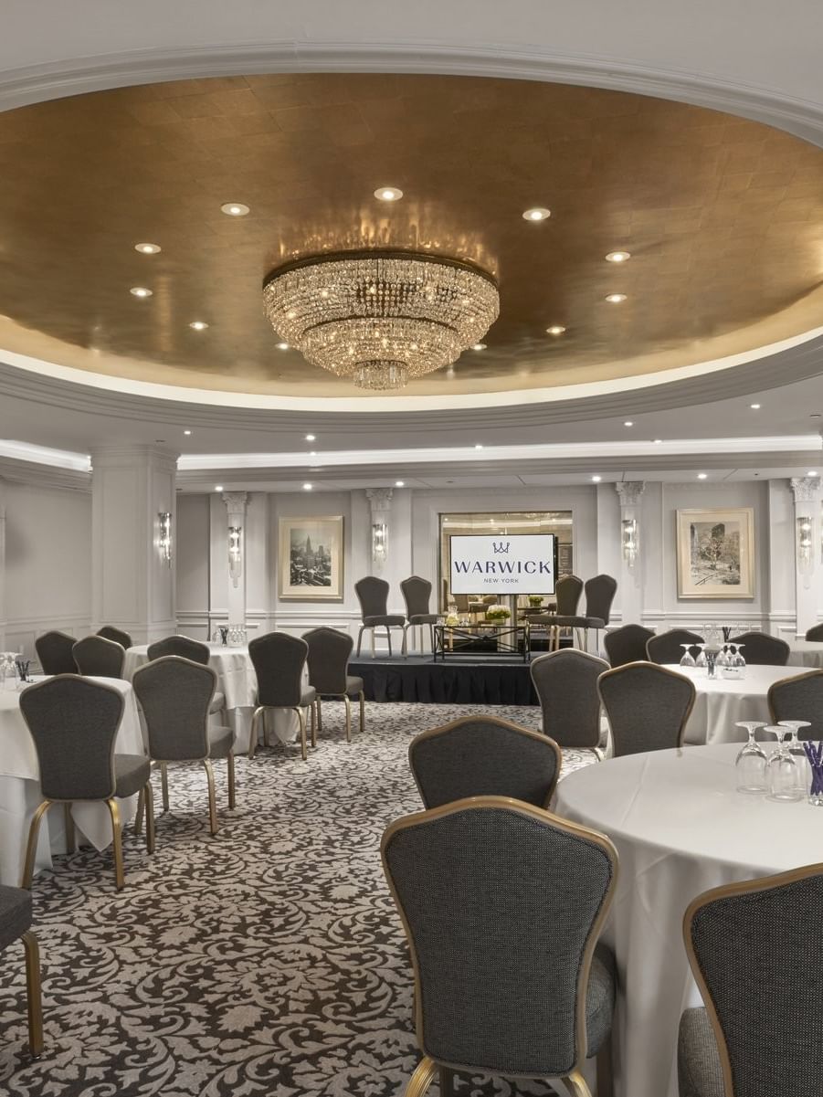 Grand ballroom with round banquet tables& chairs under a stunning gold dome and chandelier at Warwick New York