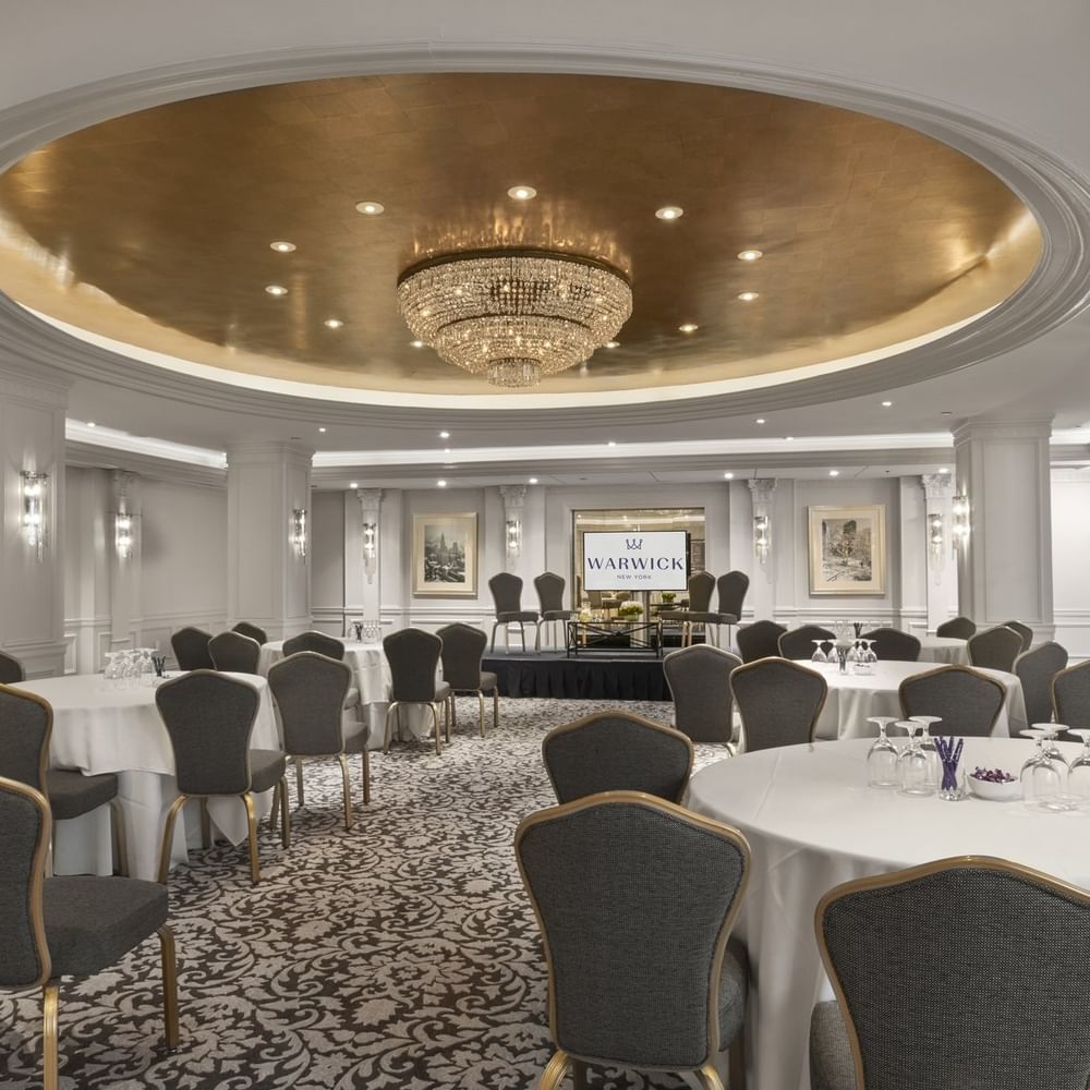 Grand ballroom with round banquet tables& chairs under a stunning gold dome and chandelier at Warwick New York