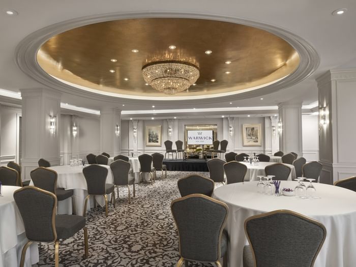 Grand ballroom with round banquet tables& chairs under a stunning gold dome and chandelier at Warwick New York