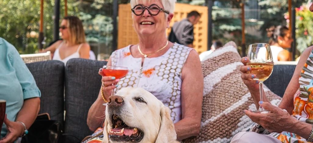 An older adult enjoys a cocktail with their dog on the patio of their hotel in Canmore.