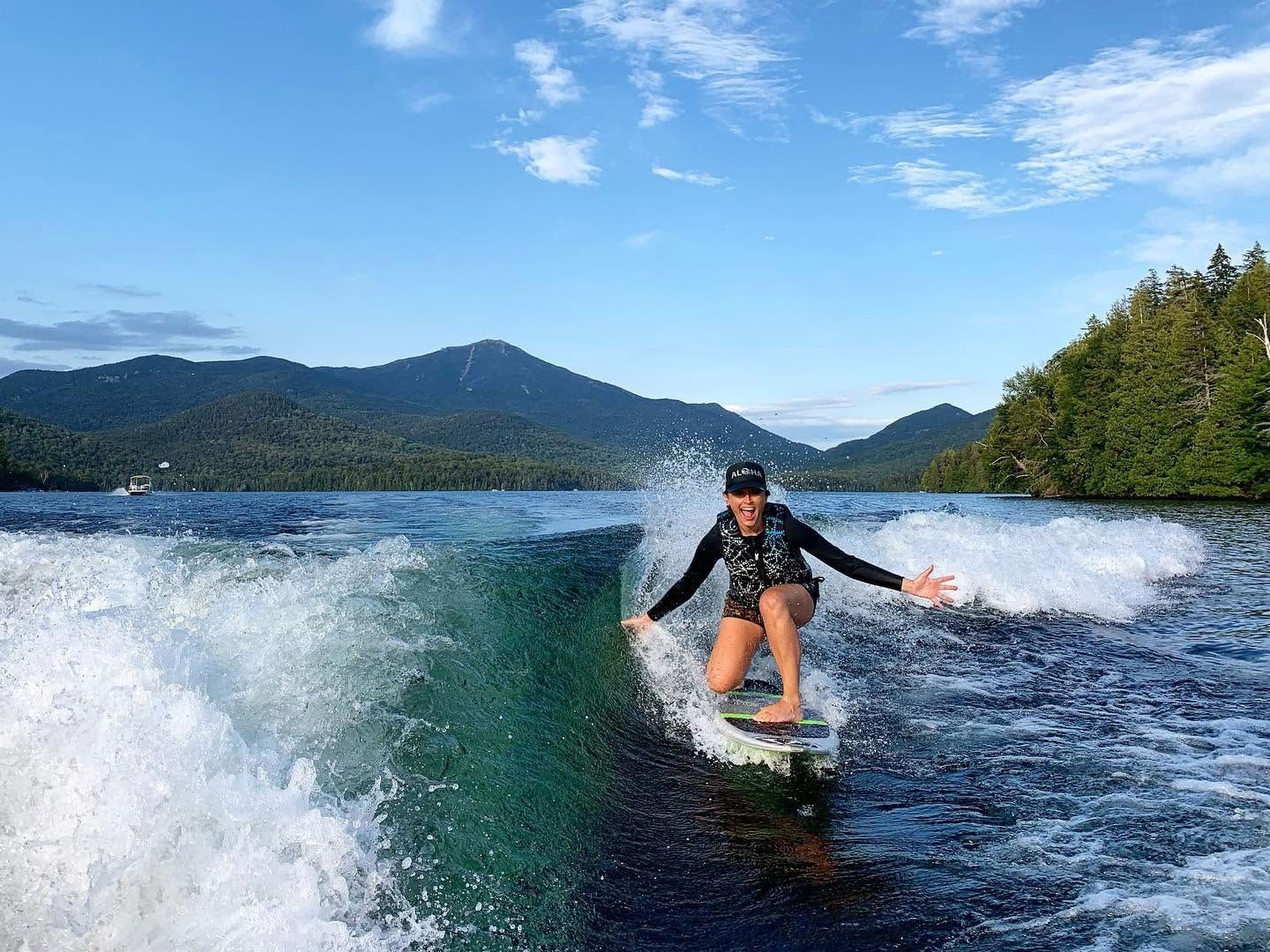 Woman wakesurfing on a lake with forested mountains in the background with ADK Aquatics