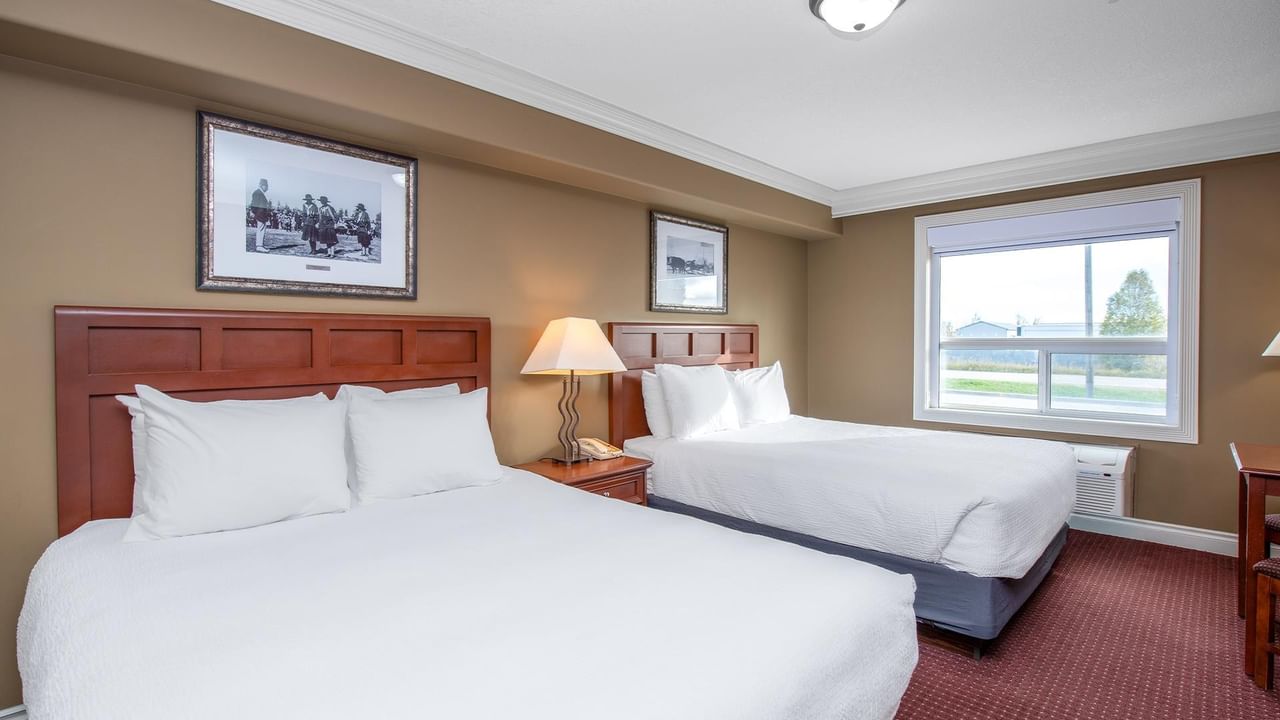 Coast Edson Hotel guest room with two beds, wooden headboards, framed artwork, and a bright window view.