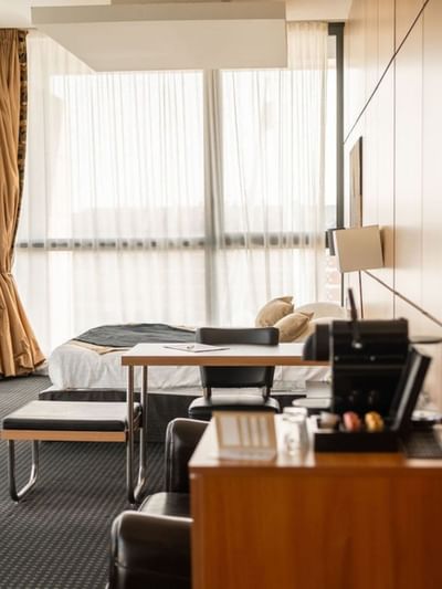 Chambre d'hôtel moderne avec lit, bureau, télévision et grandes fenêtres avec rideaux.