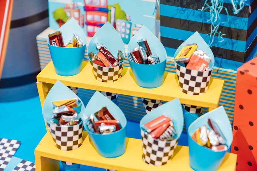 Colorful, decorative pots filled with assorted candy are neatly arranged on a bright yellow shelf at Park Hyatt Saigon