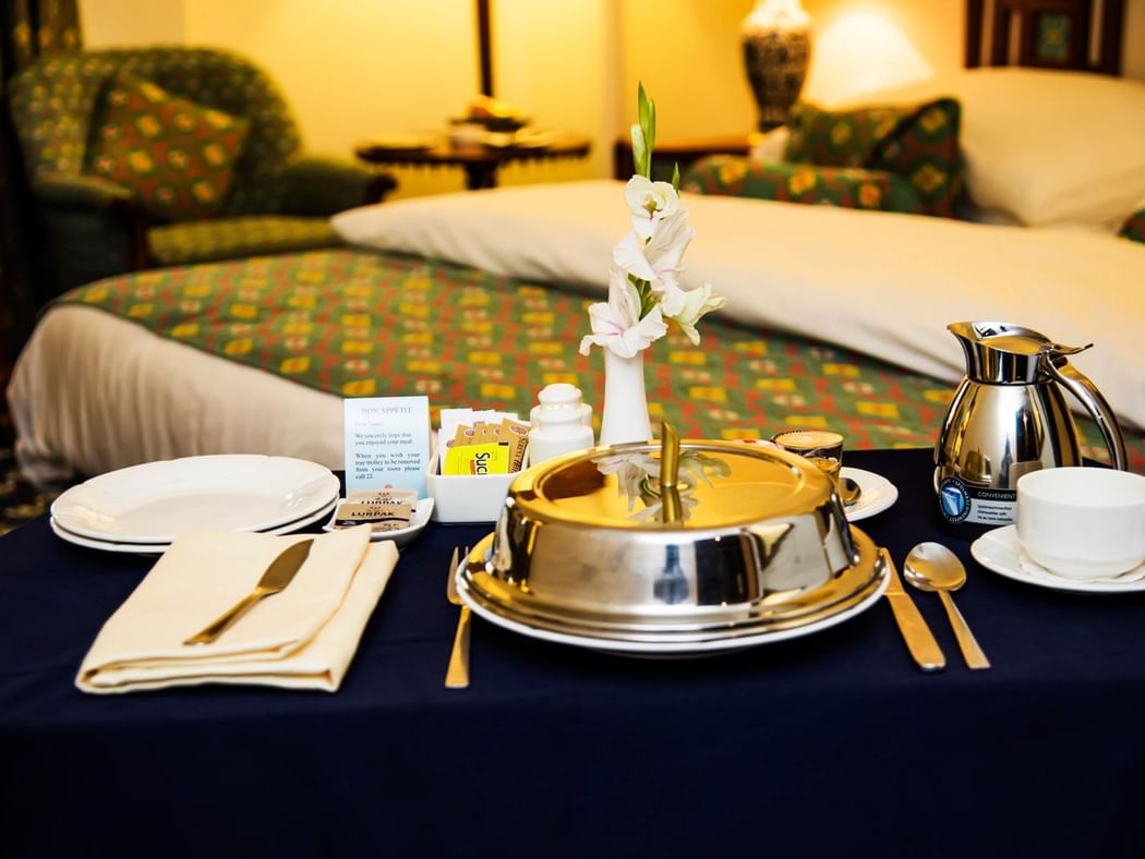 Meals on a table next to the bed at Faisalabad Serena Hotel